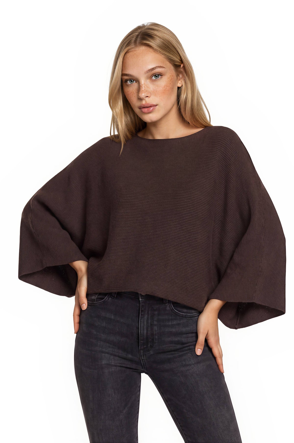 Women's dark brown ribbed knit cape sweater top with wide, draped sleeves, a boat neck and dark gray jeans.