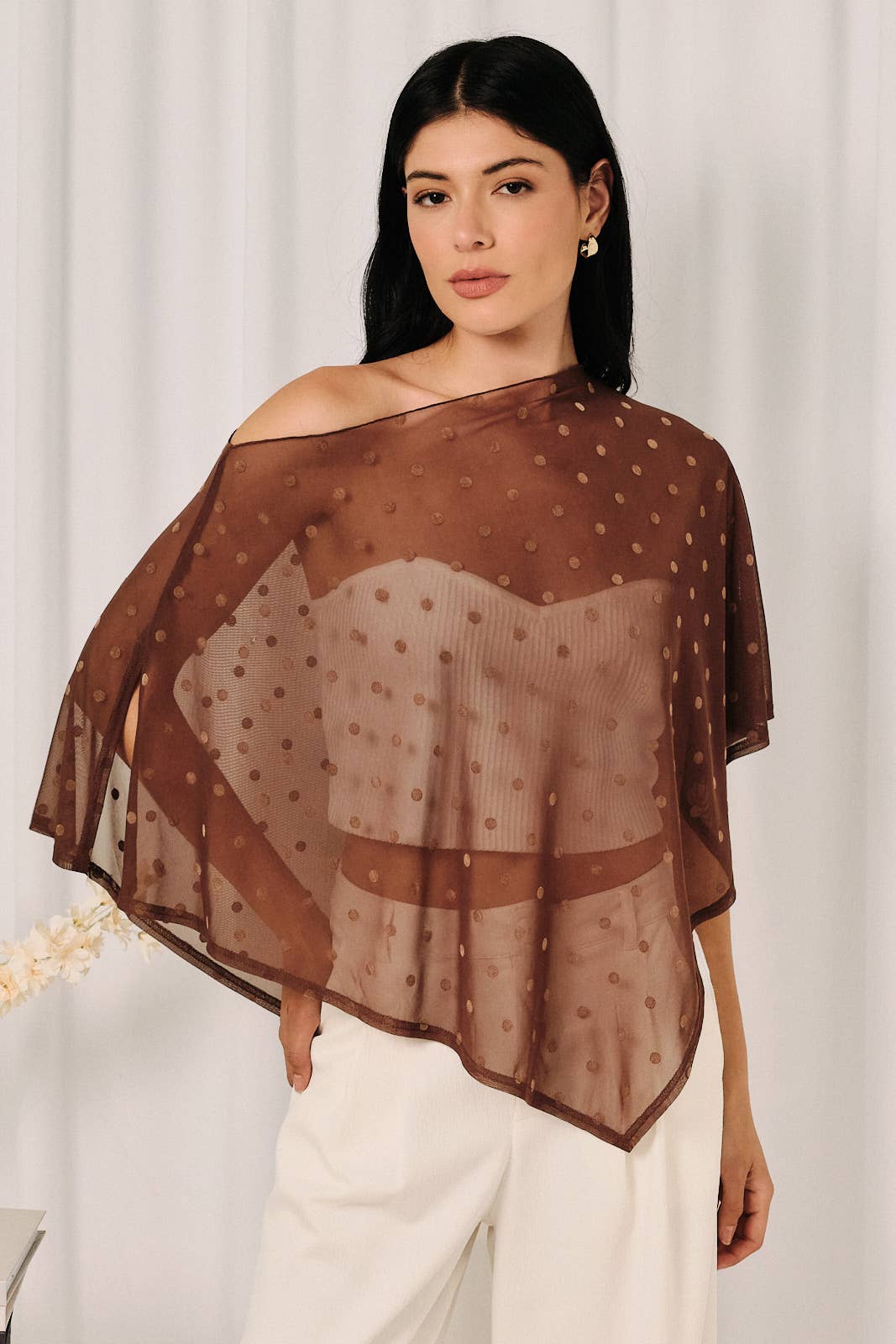 Women wearing a sheer polka dot poncho blouse with white pants. Featuring sheer brown polka dot fabric.  Sheer mesh with flocked polkadots, poncho style blouse, Boat neck, Asymmetrical hem, flowy draped silhouette. Fall fashion